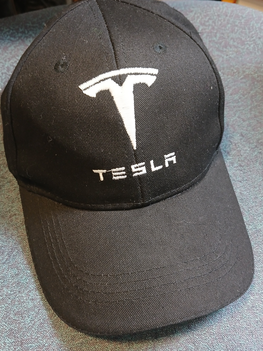 black baseball cap featuring a white embroidered Tesla logo and lettering